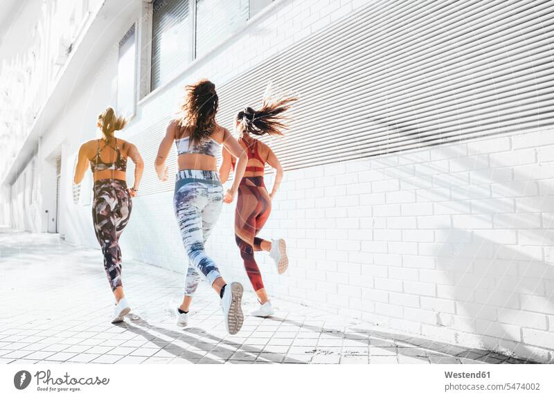 Rückansicht von drei sportlichen jungen Frauen, die in der Stadt laufen Freunde Kameradschaft Freundin rennen sommerlich Sommerzeit fit gesund Gesundheit Muße