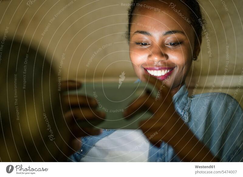 Porträt einer glücklichen jungen Frau, die nachts ein Smartphone benutzt, Lissabon, Portugal Leute Menschen People Person Personen Afrikanisch