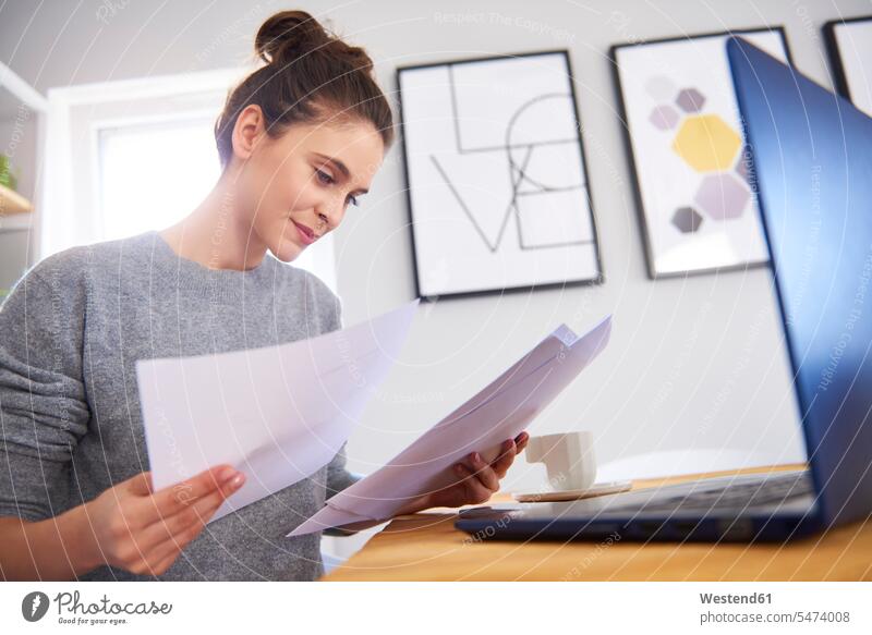 Junge Frau, die von zu Hause aus arbeitet, Laptop benutzt und Zeitung liest Europäer Kaukasier Europäisch kaukasisch Notebook Laptops Notebooks Technologie