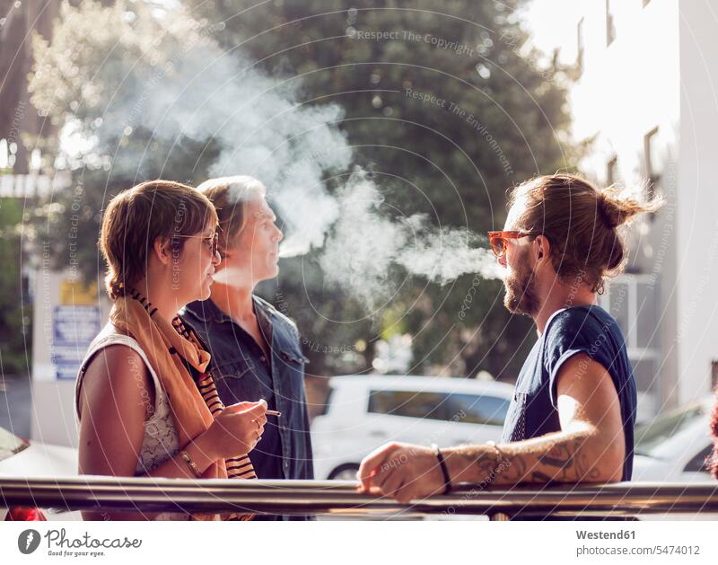 Freunde rauchen, während sie an einem sonnigen Tag im Freien stehen Farbaufnahme Farbe Farbfoto Farbphoto Außenaufnahme außen draußen Tageslichtaufnahme
