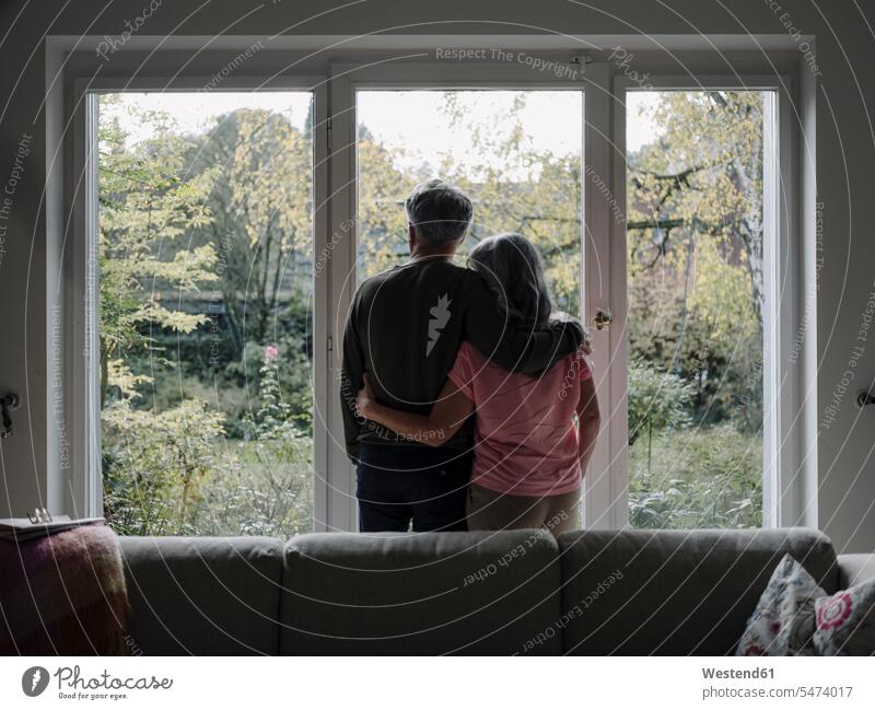 Rückansicht eines älteren Ehepaares, das zu Hause aus dem Fenster schaut Couch Couches Liege Sofas entspannen relaxen Arm umlegen Umarmung Umarmungen
