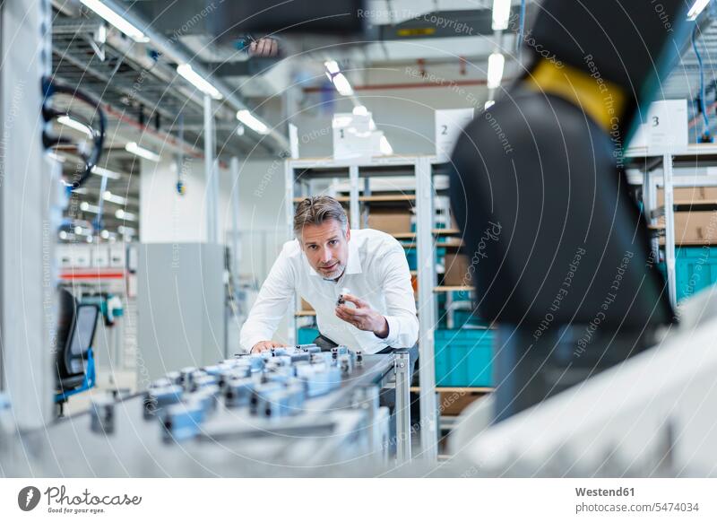 Geschäftsmann in einer modernen Fabrikhalle beim Prüfen von Werkstücken Job Berufe Berufstätigkeit Beschäftigung Jobs geschäftlich Geschäftsleben Geschäftswelt