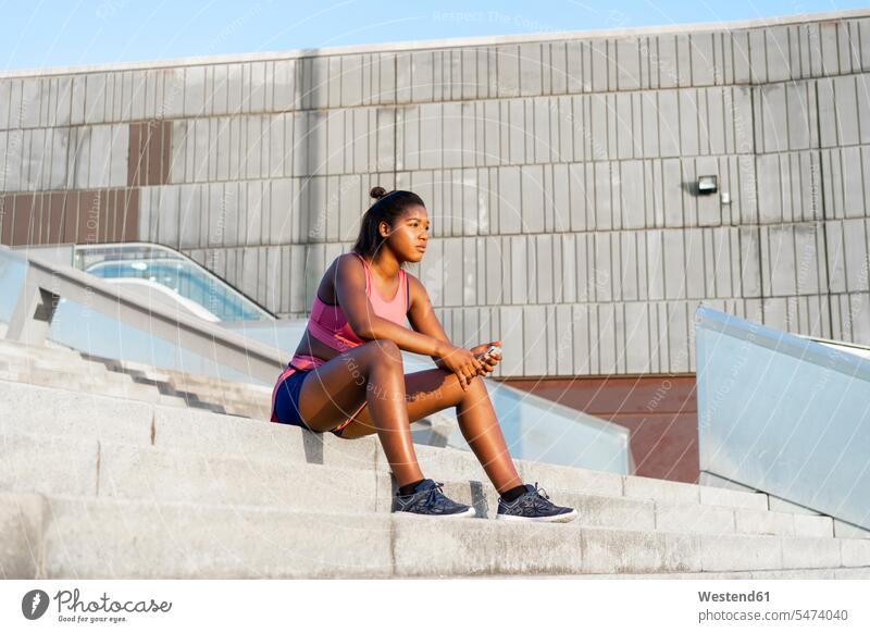 Junge sportliche Frau mit Smartphone auf Schritt und Tritt sitzend Sportlerin Sportlerinnen Workout weiblich Frauen iPhone Smartphones schlechte Nachrichten
