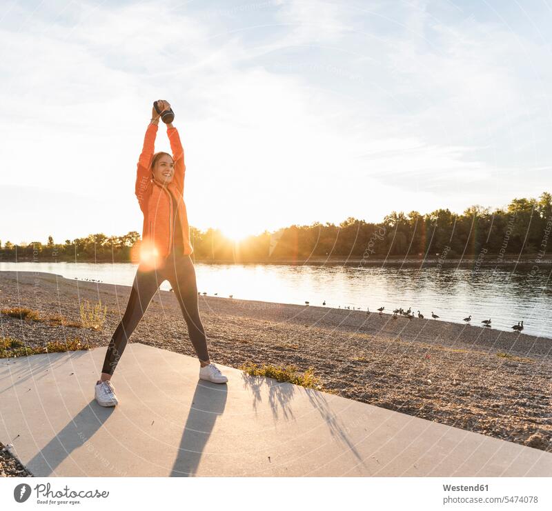 Junge Frau trainiert mit einer Kettlebell am Fluss junge Frau junge Frauen Rundgewicht Kugelhantel Kettlebells Fluesse Fluß Flüsse trainieren Fitness fit