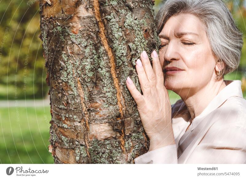Frau mit geschlossenen Augen umarmt Baum, während sie im Park steht Farbaufnahme Farbe Farbfoto Farbphoto Außenaufnahme außen draußen im Freien Tag