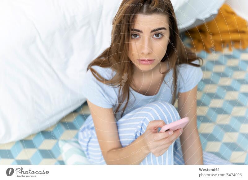 Porträt einer jungen Frau, die ein Smartphone im Schlafzimmer hält hilflos Hilflosigkeit Betten Telekommunikation telefonieren Handies Handys Mobiltelefon