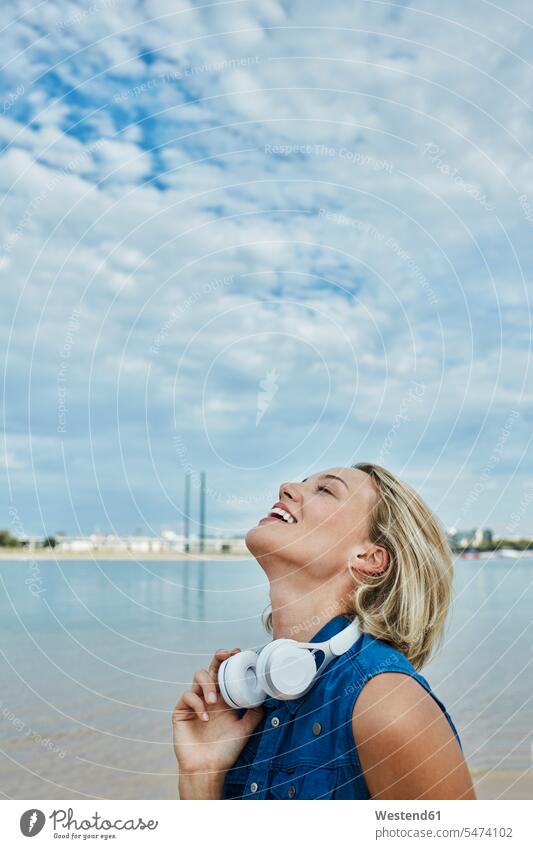 Deutschland, Düsseldorf, glückliche junge Frau mit Kopfhörer am Rheinufer Kopfhoerer weiblich Frauen Flussufer Fluesse Fluß Flüsse Glück glücklich sein
