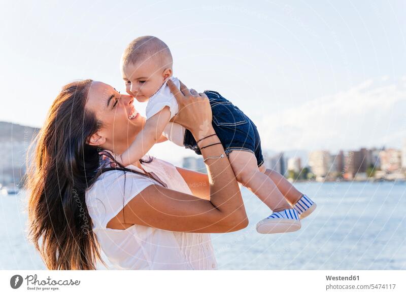 Lächelnde Mutter holt kleinen Sohn ab, während sie bei Sonnenuntergang am Meer steht Farbaufnahme Farbe Farbfoto Farbphoto Spanien Freizeitbeschäftigung Muße