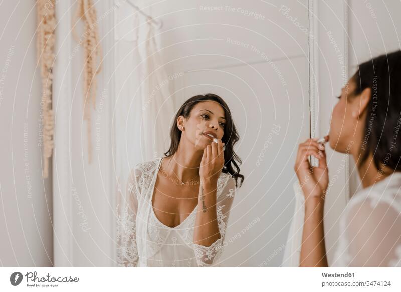Junge Braut trägt Lippenstift auf, während sie zu Hause in den Spiegel schaut Farbaufnahme Farbe Farbfoto Farbphoto Innenaufnahme Innenaufnahmen innen drinnen