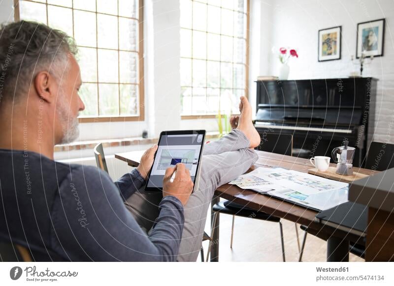 Reifer Mann arbeitet vom Heimbüro aus mit den Füßen nach oben und benutzt ein Tablett sitzen sitzend sitzt Tablet Computer Tablet-PC Tablet PC iPad