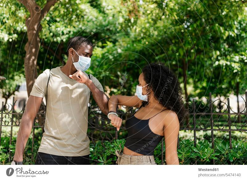 Mann und Frau tragen Masken, während sie sich im Park mit Ellbogenberührung grüßen Farbaufnahme Farbe Farbfoto Farbphoto Außenaufnahme außen draußen im Freien