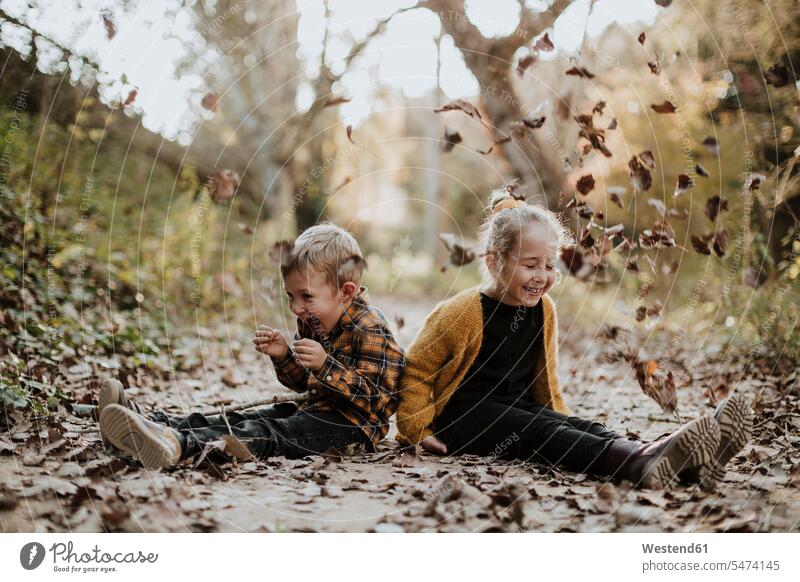 Fröhliche Mädchen und Jungen spielen mit trockenen gefallenen Blatt beim Sitzen auf Fußweg im Wald Farbaufnahme Farbe Farbfoto Farbphoto Außenaufnahme außen