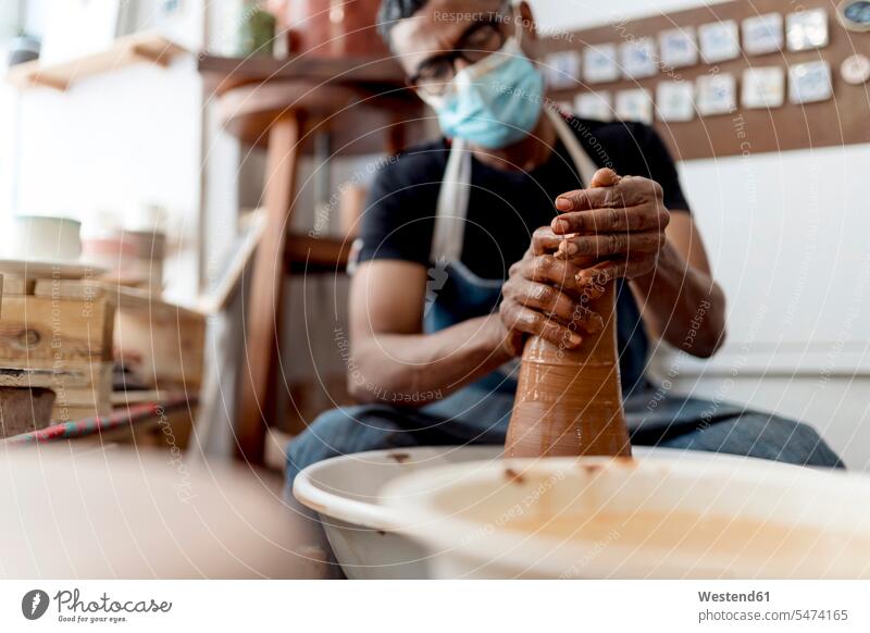 Männlicher Töpfer mit Maske, der in der Werkstatt sitzend eine Form aus Ton formt Farbaufnahme Farbe Farbfoto Farbphoto Spanien Innenaufnahme Innenaufnahmen