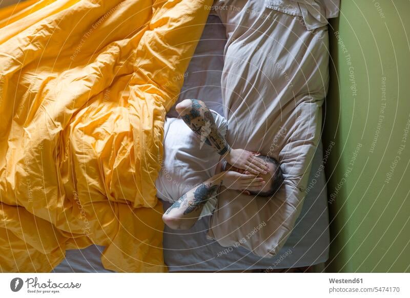 Tätowierter Mann im Bett liegend, Hände auf den Augen Leute Menschen People Person Personen Europäisch Kaukasier kaukasisch erwachsen Erwachsene Männer männlich