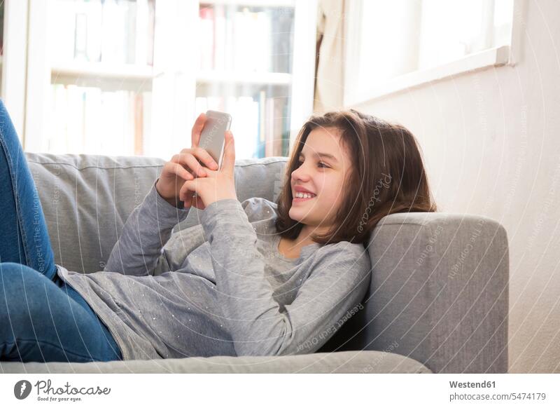 Lächelndes Mädchen liegt zu Hause auf der Couch und benutzt ein Mobiltelefon Smartphone iPhone Smartphones weiblich lächeln Sofa Couches Liege Sofas benutzen