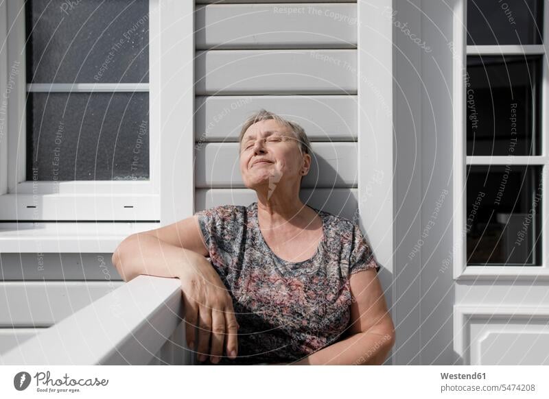 Entspannte ältere Frau sitzt auf Veranda im Sonnenschein Deutschland Wohnen ausruhen Rast Erholung erholen Wohnung wohnen Wohnungen Auszeit