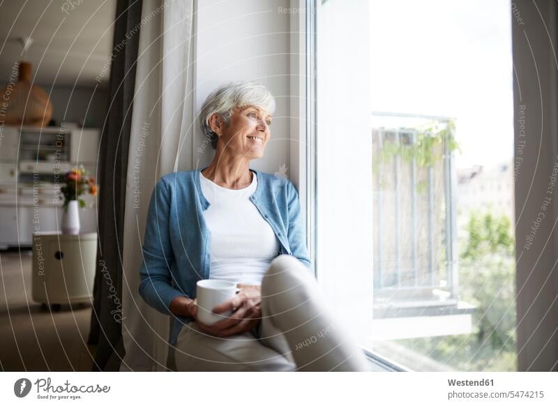 Ältere Frau, die aus dem Fenster schaut, während sie zu Hause sitzt Farbaufnahme Farbe Farbfoto Farbphoto Innenaufnahme Innenaufnahmen innen drinnen Tag