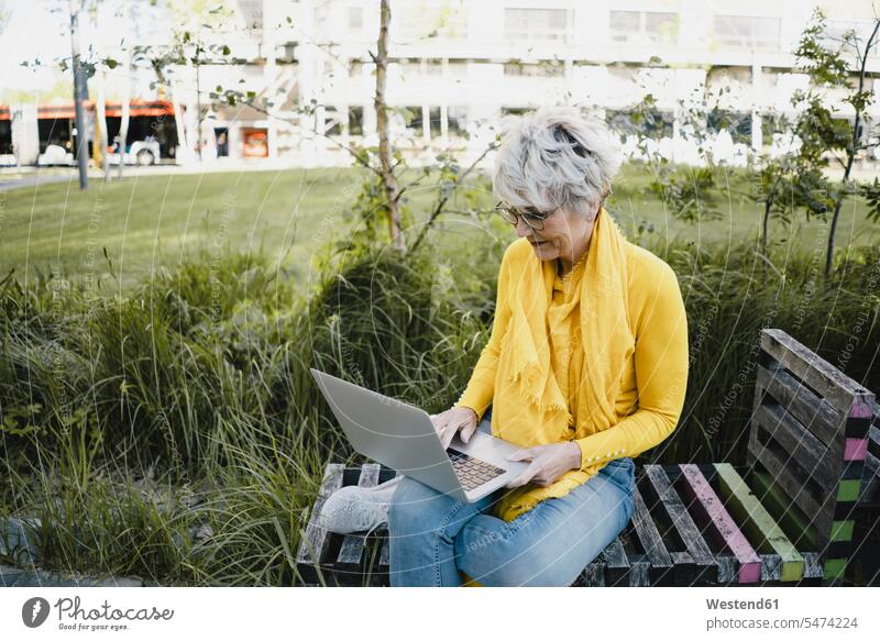 Reife Frau sitzt auf Bank im Freien und benutzt Laptop Leute Menschen People Person Personen Alleinstehende Alleinstehender Singles Unverheiratete