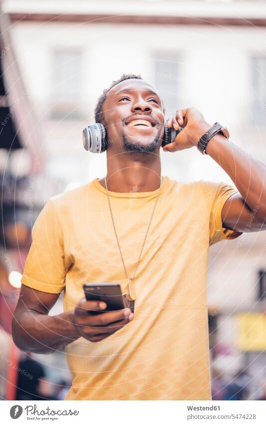 Porträt eines glücklichen Mannes, der mit Kopfhörer und Smartphone Musik hört T-Shirts Schmuckstueck Schmuckstuecke Schmuckstück Schmuckstücke Ketten Halsketten
