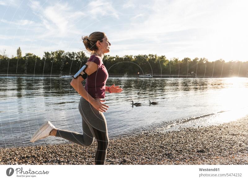 Junge Frau joggt am Fluss Joggen Jogging laufen rennen Fluesse Fluß Flüsse Fitness fit Gesundheit gesund Sport Gewässer Wasser Ganzkörperansicht Ganzansicht