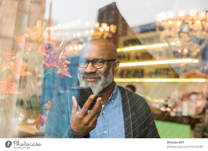 Porträt eines lächelnden Mannes mit Mobiltelefon hinter einer Fensterscheibe Fensterscheiben Smartphone iPhone Smartphones Portrait Porträts Portraits Männer