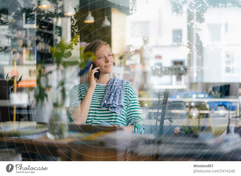 Lächelnde junge Frau am Handy in einem Cafe Kaffeehaus Bistro Cafes Café Cafés Kaffeehäuser weiblich Frauen lächeln Mobiltelefon Handies Handys Mobiltelefone