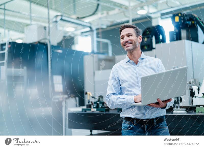 Happy reifen Geschäftsmann hält Laptop während der Arbeit in der Industrie Innenaufnahme Innenaufnahmen innen drinnen Deutschland Vorderansicht Frontalansicht
