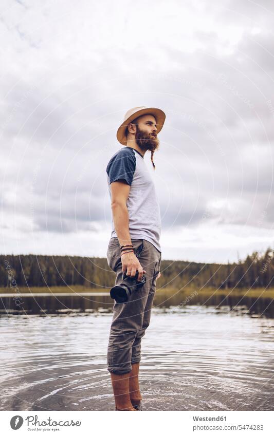 Schweden, Lappland, Mann mit Kamera steht im Wasser und schaut in die Ferne Gewässer Fotoapparat Fotokamera Kameras stehen stehend Männer männlich schauen