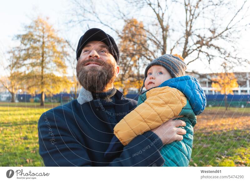 Glücklicher Mann mit seinem kleinen Sohn im Park Jacken Mützen freuen behüten behütet geborgen Sicherheit geniessen Genuss glücklich sein glücklichsein
