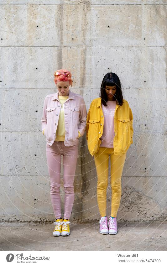 Zwei alternative Freunde, die Spaß haben, gelbe und rosa Jeans-Kleidung tragen und nach unten schauen Freundinnen Pose posieren homosexuell Homosexualität