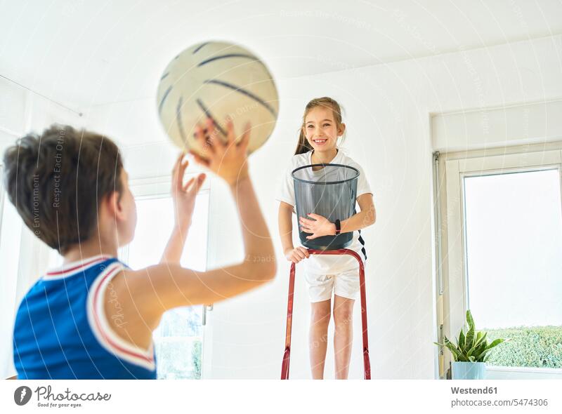 Junge und Mädchen spielen zu Hause Basketball Leitern Bälle freuen Frohsinn Fröhlichkeit Heiterkeit Glück glücklich sein glücklichsein zufrieden stehend steht