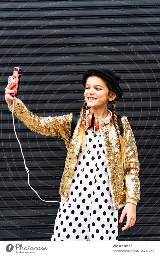 Porträt eines lächelnden Mädchens mit Hut und goldener Paillettenjacke, das ein Selfie mit seinem Smartphone macht Selfies iPhone Smartphones weiblich Portrait