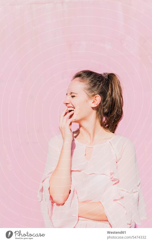 Lachende junge Frau vor rosa Wand Wände Waende weiblich Frauen rosafarben lachen Erwachsener erwachsen Mensch Menschen Leute People Personen Farbe Farbtöne