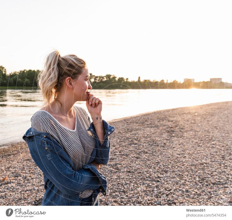 Junge blonde Frau wartet abends am Flussufer warten Abend nachdenklich stehen stehend steht weiblich Frauen Seitenblick Blick zur Seite Ufer Erwachsener