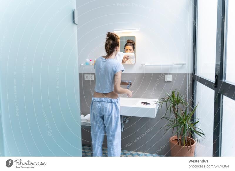 Rückansicht einer jungen Frau beim Zähneputzen im Badezimmer Handtuecher Handtücher Zahnbürsten Telekommunikation telefonieren Handies Handys Mobiltelefon