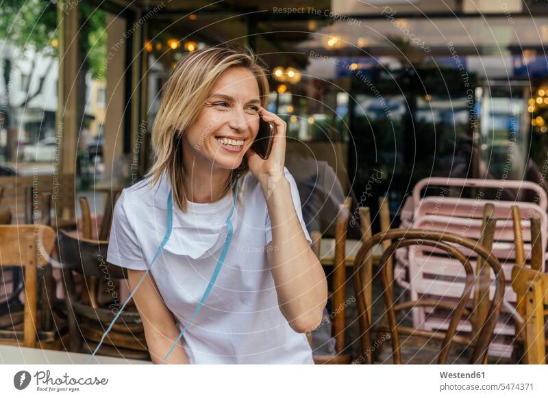 Porträt einer Frau am Telefon mit Schutzmaske vor einem geschlossenen Café Fensterscheiben Bänder T-Shirts Telekommunikation telefonieren Handies Handys