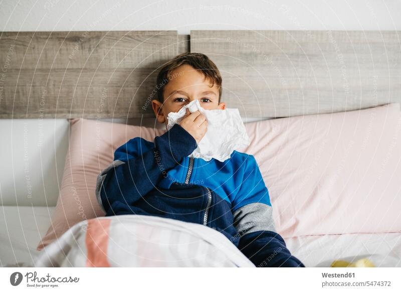 Porträt eines kranken Jungen, der im Bett liegt und sich die Nase schnäuzt Hygieneartikel Taschentuecher Taschentücher daheim zu Hause frontal Frontalansicht