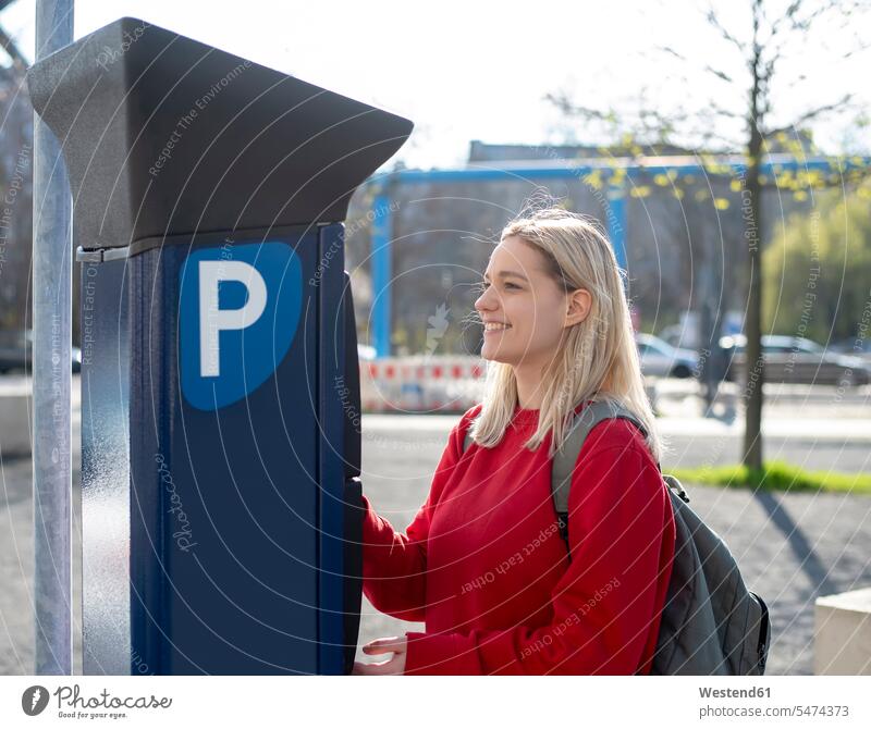 Lächelnde junge Frau, die einen Kassenautomaten benutzt Rucksack Rucksäcke benutzen benützen optimistisch Optimismus Städtisches Motiv staedtisch