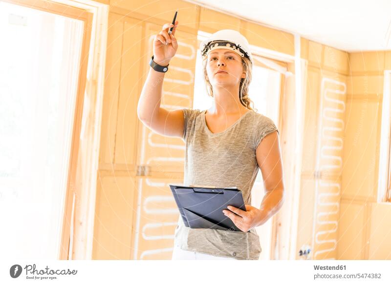 Junge Frau prüft den Bau eines neuen Holzhauses Job Berufe Berufstätigkeit Beschäftigung Jobs Arbeiter Helme aufschreiben notieren schreibend Schrift stehend