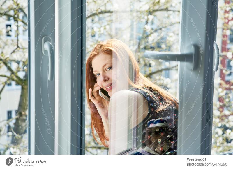 Porträt einer rothaarigen Frau am Telefon, die sich im Frühling aus dem Fenster lehnt Portrait Porträts Portraits rote Haare rotes Haar rothaariger rothaariges