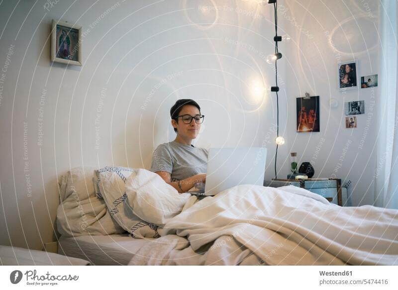 Junge Frau sitzt im Bett, mit Laptop ansehen betrachten betrachtend Laptop benutzen Laptop benützen junge Frau junge Frauen Zuhause zu Hause daheim sitzen