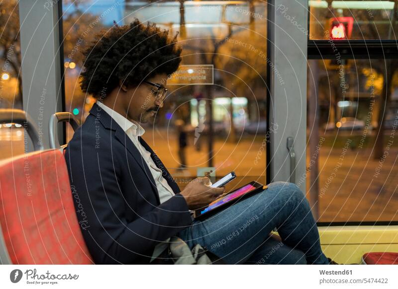 Spanien, Barcelona, Geschäftsmann in einer Straßenbahn bei Nacht mit Handy und Tablet nachts Tablet Computer Tablet-PC Tablet PC iPad Tablet-Computer