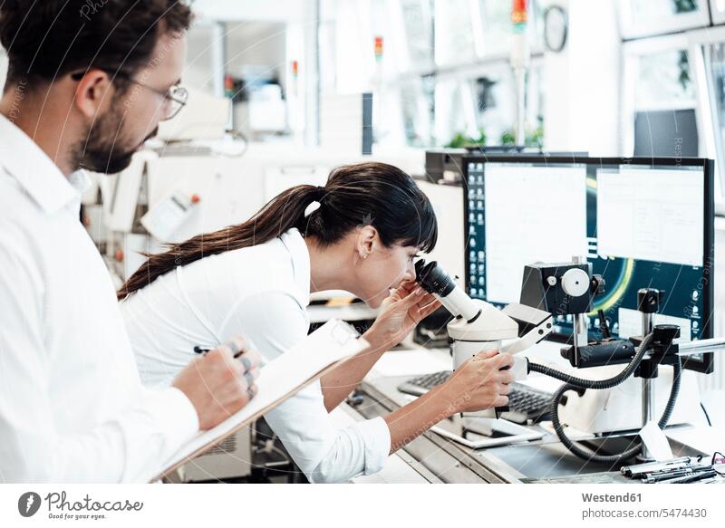Weibliche Geschäftsfrau schaut durch das Mikroskop, während sie einem männlichen Kollegen im Labor zur Seite steht Farbaufnahme Farbe Farbfoto Farbphoto