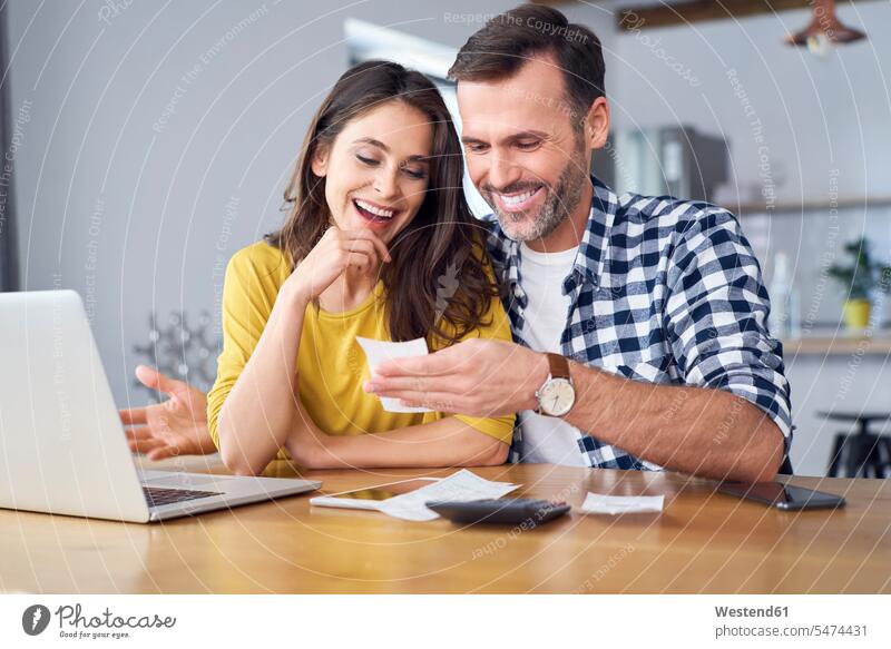 Paar, das am Esstisch sitzt, einen Laptop benutzt und Rechnungen überprüft Laptop benutzen Laptop benützen sitzen sitzend Tisch Tische Zuhause zu Hause daheim