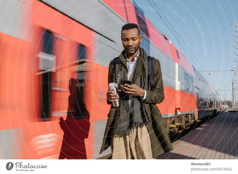 Porträt eines stilvollen Mannes, der sein Smartphone neben einem Zug benutzt geschäftlich Geschäftsleben Geschäftswelt Geschäftsperson Geschäftspersonen