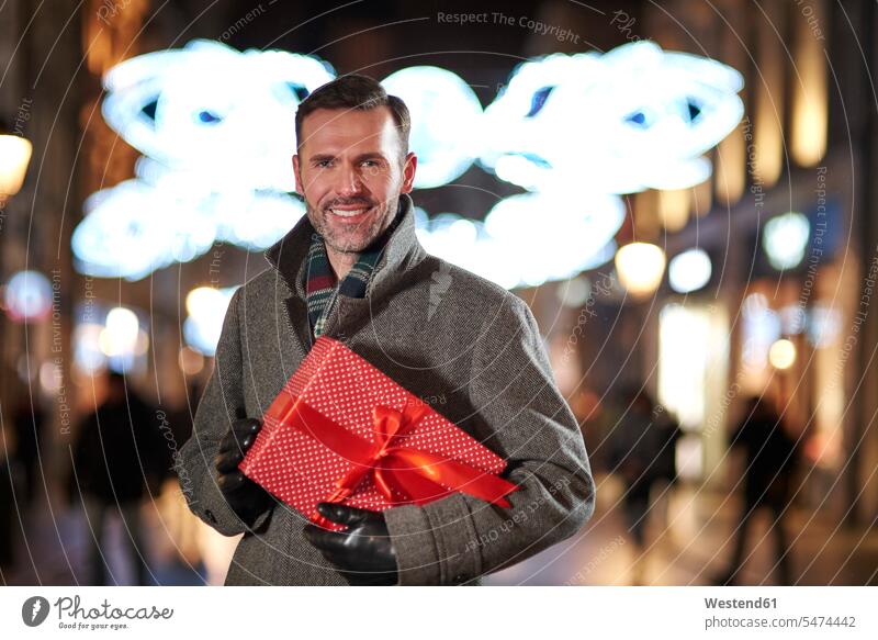 Porträt eines lächelnden Mannes mit Weihnachtsgeschenk in der Fußgängerzone am Abend abends Fussgängerzone Fußgängerzonen Fussgaengerzone Fussgängerzonen