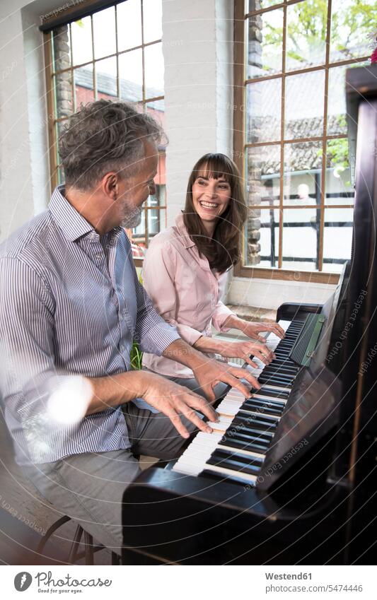 Ein reifes Paar, das sich zu Hause amüsiert und Klavier spielt Spaß Spass Späße spassig Spässe spaßig Pärchen Paare Partnerschaft Piano Pianos Klaviere spielen