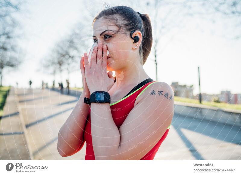 Sportliche junge Frau mit schnurlosen Kopfhörern, die sich die Nase schnäuzt Uhren Armbanduhren Taschentuecher Taschentücher hoeren Farben Farbtoene Farbton
