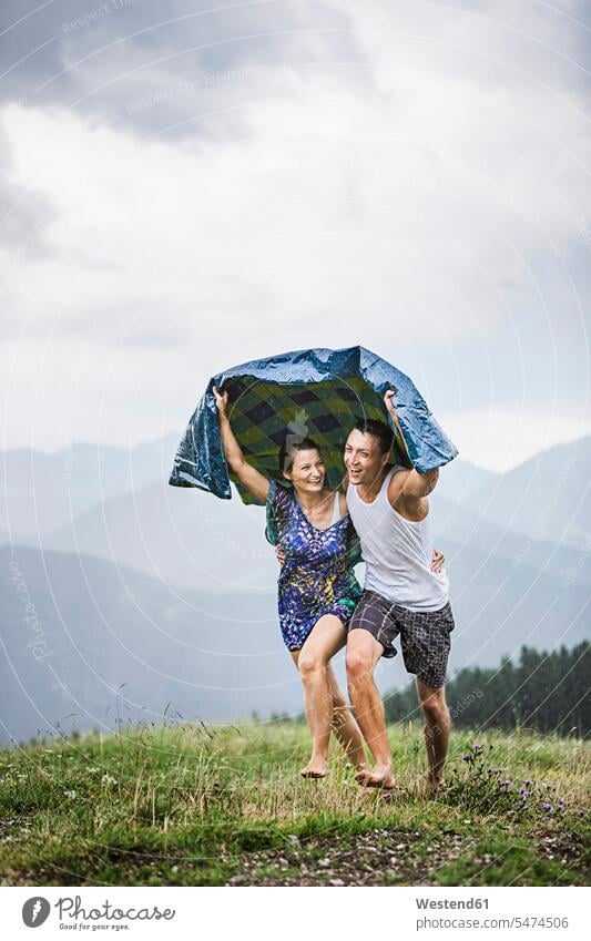 Glückliches Paar läuft bei Regen auf einer Bergwiese, Achenkirch, Österreich Decken entspannen relaxen freuen Frohsinn Fröhlichkeit Heiterkeit geniessen Genuss