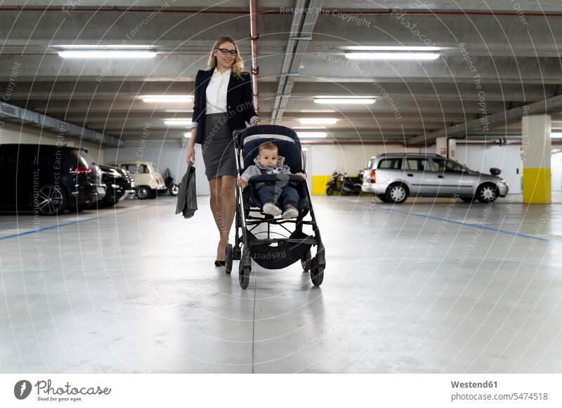 Junge Geschäftsfrau schiebt Kinderwagen mit Baby Junge auf dem Parkplatz Europäer Kaukasier Europäisch kaukasisch Familie mit einem Kind Lifestyle Lebensstil